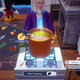 A man in a blue shirt and purple jacket cooks a meal using a large pot in Dreamlight Valley.